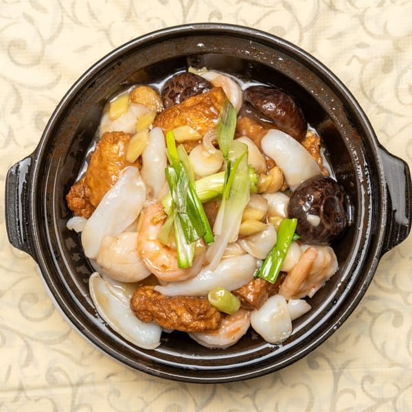 A clay pot filled with stir-fried shrimp, squid, mushrooms, tofu, and green onions.