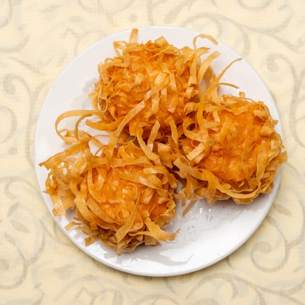 Three crispy, golden-brown fried shrimp balls with shredded pastry on a white plate.