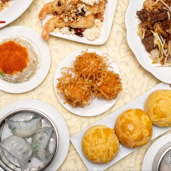 Overhead view of a table laden with various Chinese dishes, including dim sum, noodles, and fried shrimp.