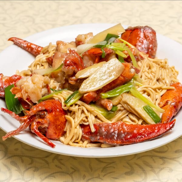 Lobster with noodles, green onions, and bamboo shoots on a white plate.