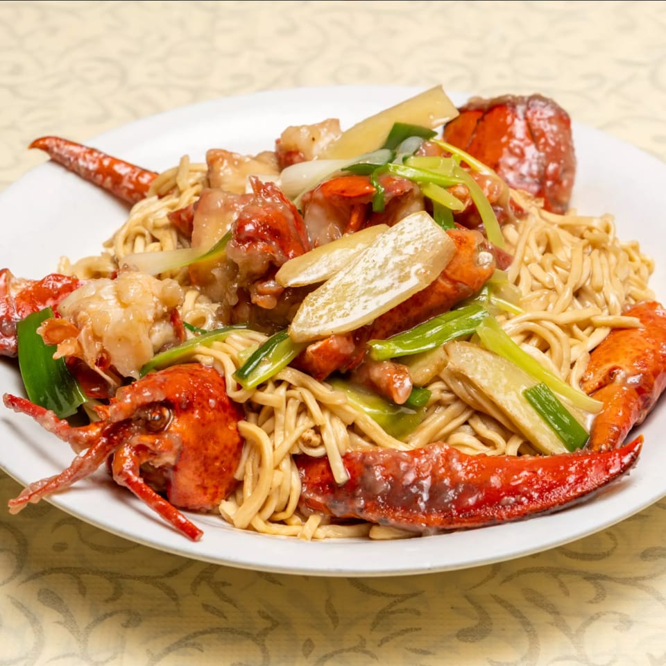 Lobster with noodles, green onions, and bamboo shoots on a white plate.