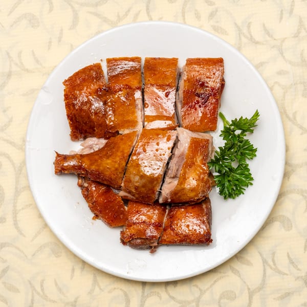 Crispy roasted duck, cut into pieces, served on a white plate with a sprig of parsley.