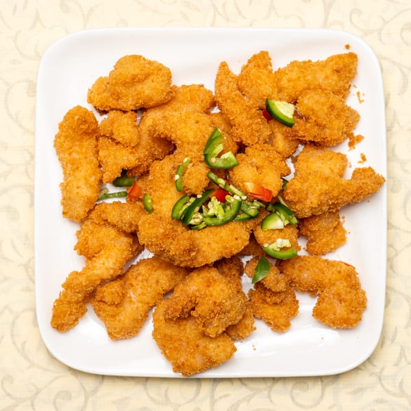 Crispy fried shrimp with sliced green and red chili peppers on a white rectangular plate.